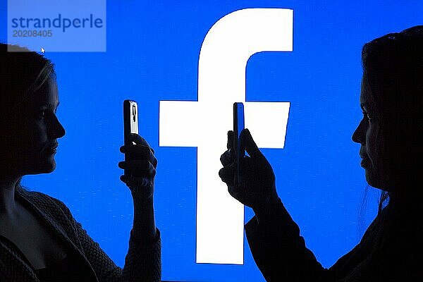 Silhouetten zweier Frauen mit Smartphones vor Facebook Logo  12.01.2016