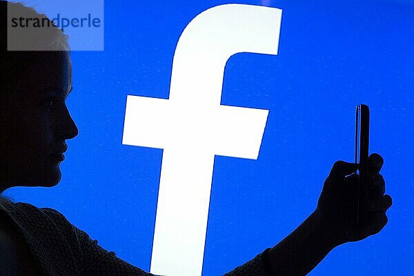 Silhouette einer Frau mit einem Smartphone in der Hand vor einem Facebook Logo  12.01.2016