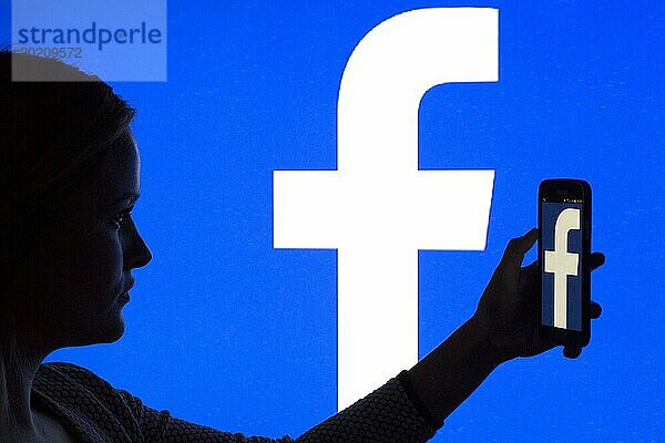 Silhouette einer Frau mit einem Smartphone in der Hand vor einem Facebook Logo  12.01.2016