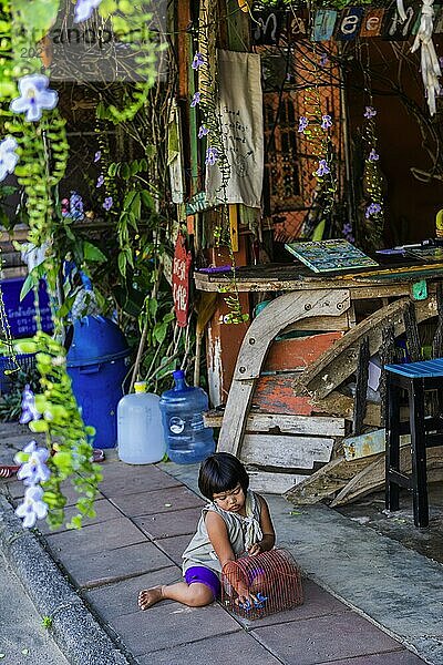 Kind spielt in einer Straßenszene in der Altstadt von Ko Lanta  marode  Stadt  urban  wohnen  leben  asiatisch  Straße  exotisch  Tourismus  Reise  Fernreise  Dorf  urban  Mädchen  spielen  Kindheit  allein  einsam  Armut  Spielszene  Emotion  Ruhe  ruhig  draußen  Traditionell  dörflich  Thailand  Asien