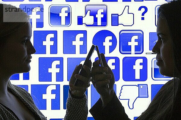 Silhouetten zweier Frauen mit Smartphones vor Facebook Logo  12.01.2016