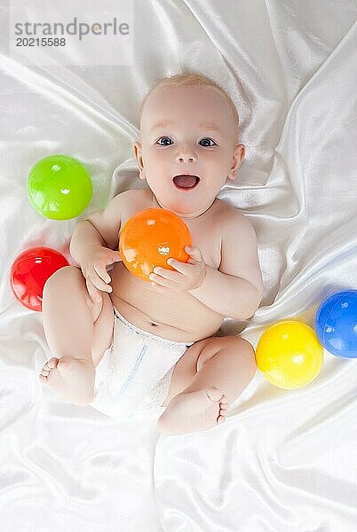 Porträt eines glücklichen Babys  das mit bunten Bällen im Bett liegt. Ansicht von oben