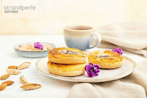 Kleine Käsekuchen mit Marmelade und Mandeln mit einer Tasse Kaffee auf weißem Betonhintergrund und Leinenstoff. Seitenansicht  Nahaufnahme  selektiver Fokus