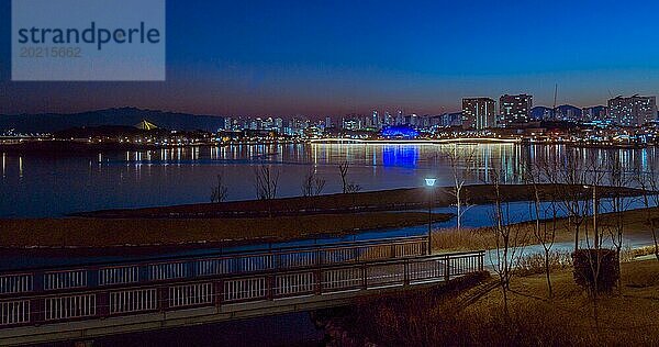 Nachtansicht eines beleuchteten Weges entlang eines ruhigen städtischen Flussufers mit Lichtern der Stadt  in Südkorea