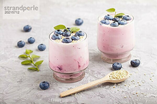 Joghurt mit Blaubeeren und Sesam in einem Glas und Holzlöffel auf grauem Betonhintergrund. Seitenansicht  Nahaufnahme