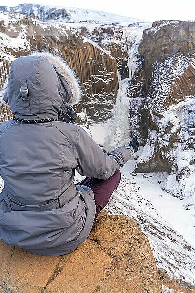 Eine Frau meditiert im Winter in Island am gefrorenen Wasserfall Hengifoss