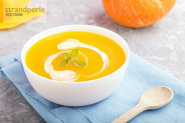 Traditionelle Kürbiscremesuppe in weißer Schale auf grauem Betonhintergrund mit blauer Serviette. Seitenansicht  Nahaufnahme  selektiver Fokus