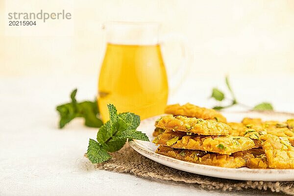 Traditionelles iranisches Dessert Sohan mit einem Glas grünem Tee auf einem grauen Betonhintergrund und Leinenstoff. Seitenansicht  Nahaufnahme  selektiver Fokus