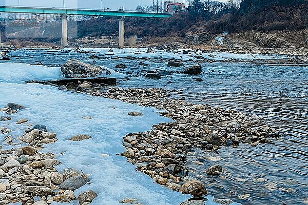 Mäandernder Fluss mit verstreuten Steinen und Eis  Brücke in der Ferne  in Südkorea