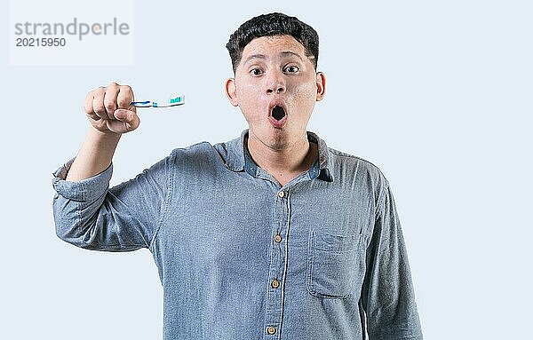 Überrascht junger Mann hält Zahnbürste mit Zahnpasta isoliert. Erstaunte Person hält Zahnbürste und schaut in die Kamera