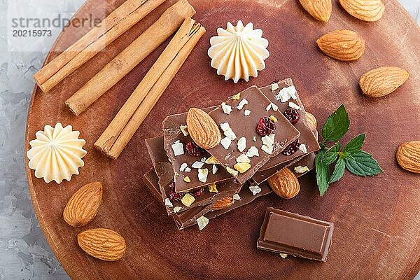 Ein Stück Milchschokolade mit Mandeln und getrockneten Früchten auf einem braunen Holzbrett auf einem grauen Betonhintergrund. Draufsicht  Nahaufnahme  selektiver Fokus  Flat Lay