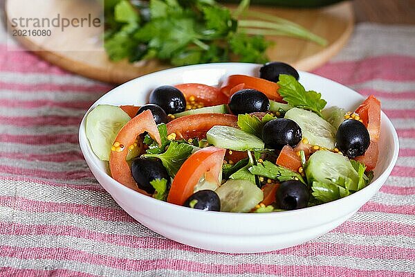 Vegetarischer Salat aus Tomaten  Gurken  Petersilie  Oliven und Senf auf Leinentischdecke  Nahaufnahme  selektiver Fokus