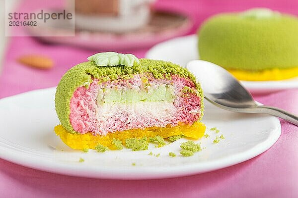 Grüner Mousse Kuchen mit Pistazien und Erdbeersahne auf weißem Holzhintergrund und rosa Stoff. Seitenansicht  Nahaufnahme  selektiver Fokus