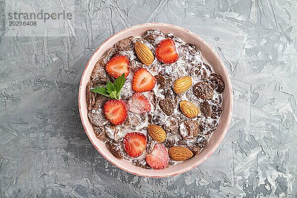 Schokoladen Cornflakes mit Milch  Erdbeeren und Mandeln in einer Keramikschale auf grauem Betonhintergrund. Draufsicht  flach gelegt  Nahaufnahme