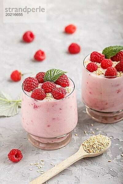 Joghurt mit Himbeere und Sesam in einem Glas und Holzlöffel auf grauem Betonhintergrund. Seitenansicht  Nahaufnahme