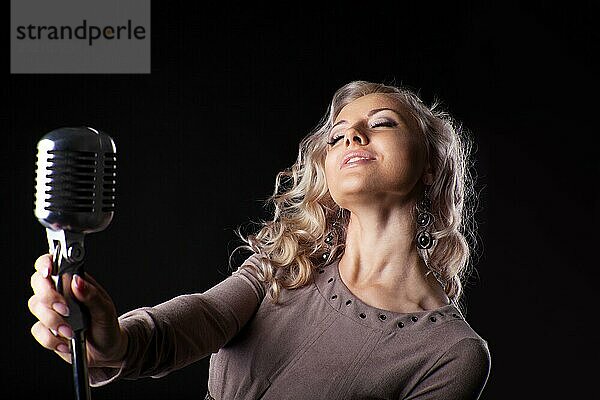 Schöne blonde Frau singt in Mikrofon mit Leidenschaft in der Dunkelheit
