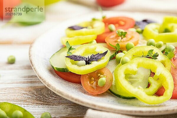 Vegetarischer Salat aus grünen Erbsen  Tomaten  Paprika und Basilikum auf weißem Holzhintergrund und Leinentuch. Seitenansicht  Nahaufnahme  selektiver Fokus