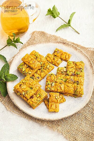 Traditionelles iranisches Dessert Sohan mit einem Glas grünem Tee auf einem grauen Betonhintergrund und Leinenstoff. Seitenansicht  Nahaufnahme  selektiver Fokus