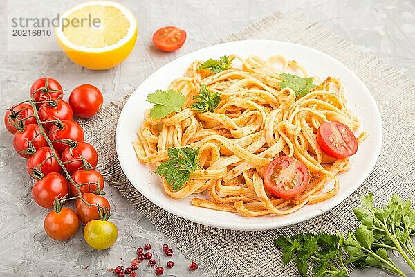 Grießnudeln mit Tomaten Pesto Sauce  Orangen und Kräutern auf einem weißen Keramikteller auf grauem Betonhintergrund. Seitenansicht  Nahaufnahme  selektiver Fokus