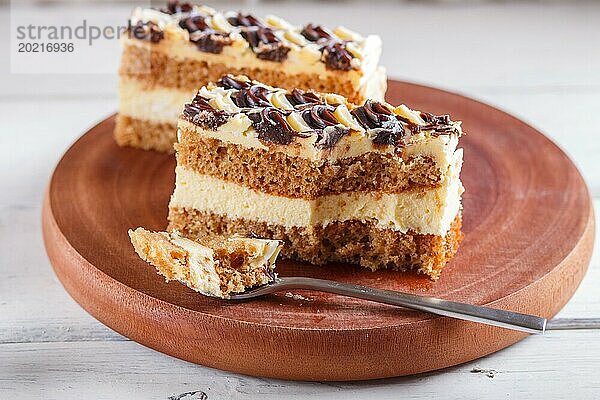 Ein Stück Kuchen mit Milch und Buttercreme  geschnitten mit einem Löffel auf einem hölzernen Küchenbrett  Nahaufnahme  selektiver Fokus  weißer Hintergrund