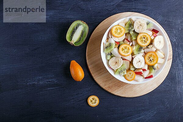 Vegetarischer Salat aus Bananen  Äpfeln  Birnen  Kumquats und Kiwi auf schwarzem woodem Hintergrund  Draufsicht  Kopierraum