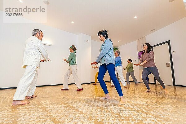 Ein männlicher Qi Gong Lehrer leitet eine Qi Gong Stunde mit reifen und erwachsenen kaukasischen Frauen