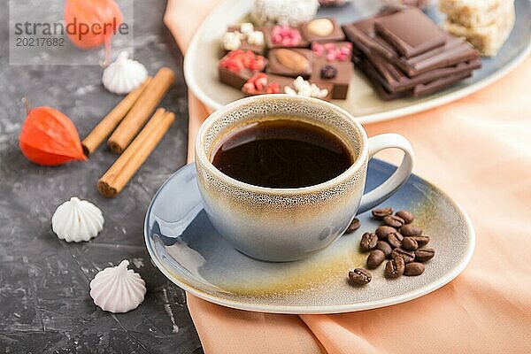 Eine Tasse Kaffee mit Schokolade und Kokosnussbonbons auf einem schwarzen Betonhintergrund und orangefarbenem Textil. Seitenansicht  Nahaufnahme  selektiver Fokus