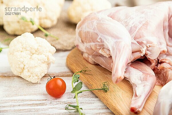 Ganzes rohes Kaninchen mit Blumenkohl  Tomaten und Gewürzen auf einem weißen Holzhintergrund und Leinenstoff. Seitenansicht  Nahaufnahme  selektiver Fokus