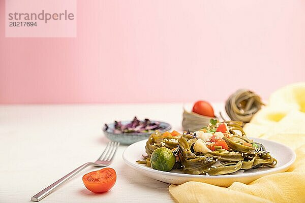 Tagliatelle mit grünem Spinat  Tomaten  Erbsen und Mikrosprossen auf weißem und rosa Hintergrund und gelbem Textil. Seitenansicht  Kopierraum  selektiver Fokus