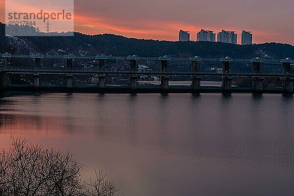 Sonnenuntergang über einem Flussdamm mit Silhouette von entfernten Gebäuden  in Südkorea