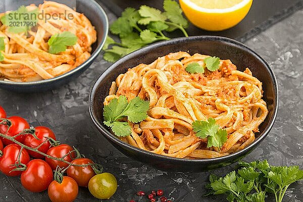 Grießnudeln mit Tomaten Pesto Soße  Orange und Kräutern in Schalen auf schwarzem Betonhintergrund. Seitenansicht  Nahaufnahme  selektiver Fokus