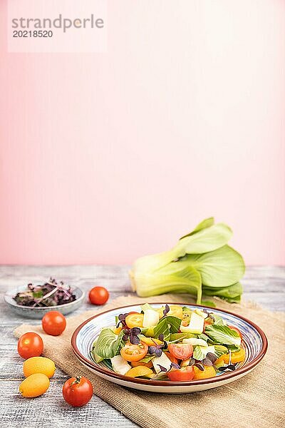 Vegetarischer Salat aus Pac Choi Kohl  Kiwi  Tomaten  Kumquat  Mikrogrünsprossen auf grauem und rosa Hintergrund und Leinentuch. Seitenansicht  Nahaufnahme  selektiver Fokus  Kopierraum