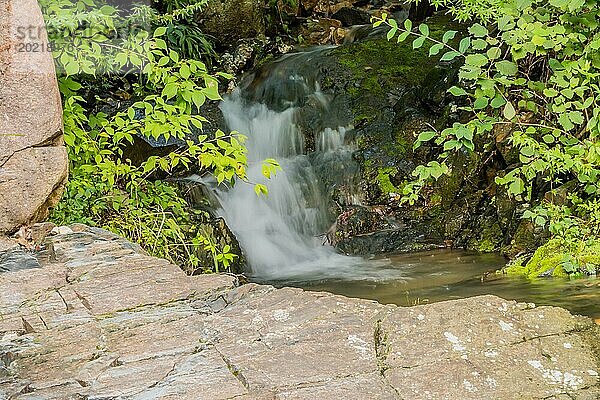 Ein ruhiger Wasserfall stürzt in Südkorea in Kaskaden über Felsen  umgeben von üppigem grünem Laub