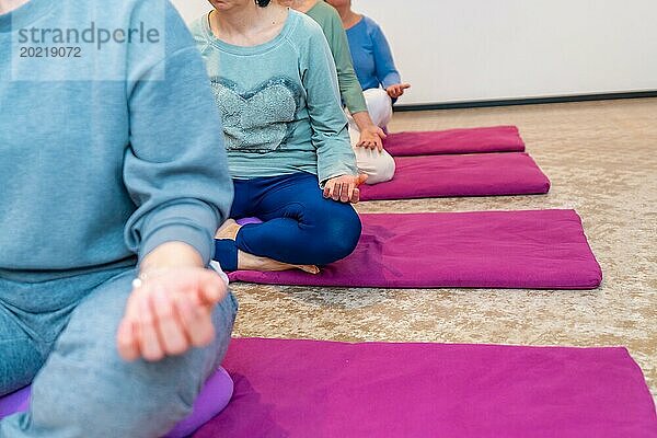 Ausgeschnittenes Foto mit Fokus auf die Hände von Frauen im Lotussitz beim Yoga in einer Klasse