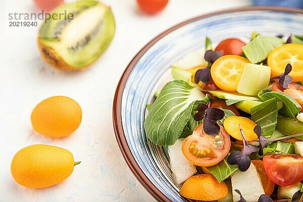 Vegetarischer Salat aus Pac Choi Kohl  Kiwi  Tomaten  Kumquat  Mikrogrünsprossen auf weißem Betonhintergrund und blauem Leinentuch. Seitenansicht  Nahaufnahme  selektiver Fokus