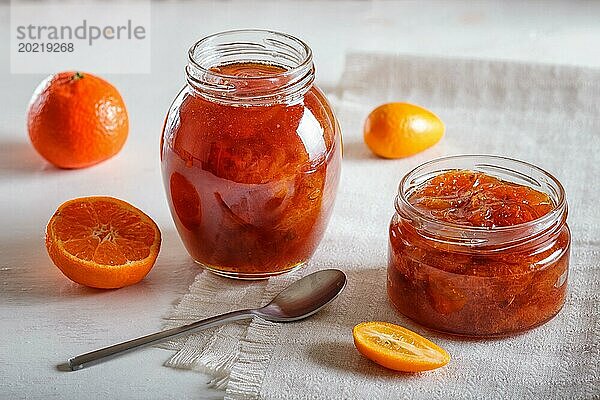 Mandarinen und Kumquatmarmelade in einem Glas mit frischen Früchten auf weißem Hintergrund. Hausgemacht  Nahaufnahme