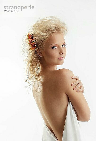 Schöne nackte junge Frau mit Blume im blonden Haar