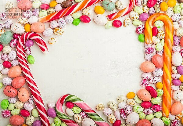 Bunte Rahmen von bunten Bonbons auf einem weißen hölzernen Hintergrund. Weihnachtsstangen  Schokoladeneier  Karamell Dragees. Kreis Kopierraum  Draufsicht  flach legen
