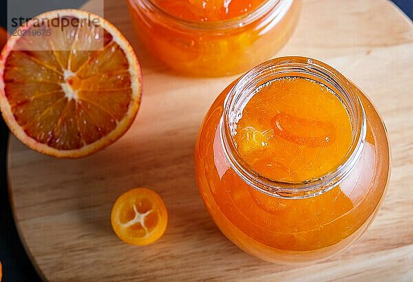 Orangen und Kumquatmarmelade in einem Glas mit frischen Früchten auf einem Küchenbrett aus Holz. Hausgemacht  Nahaufnahme  Draufsicht