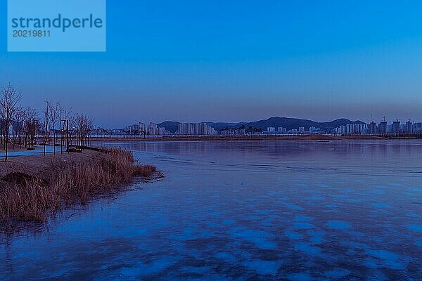 Heitere Morgendämmerung mit der Skyline einer Stadt am Wasser und Eis im Vordergrund  in Südkorea