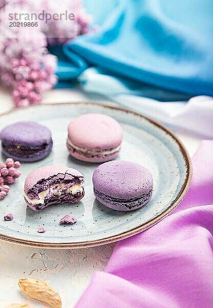 Lila Makronen oder Makronen Kuchen mit Tasse Kaffee auf einem weißen Beton Hintergrund und magenta blauen Textil. Seitenansicht  Nahaufnahme  selektiver Fokus