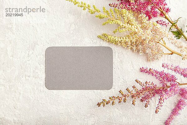 Graues Papier Visitenkarte Mockup mit lila Astilbe Blumen auf grauem Beton Hintergrund. Leer  Draufsicht  Kopierraum  Stillleben. Frühlingskonzept