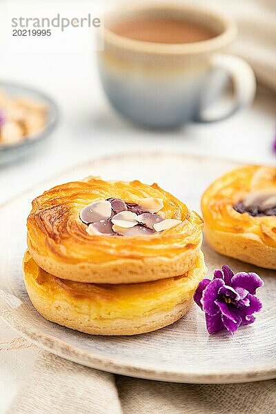 Kleine Käsekuchen mit Marmelade und Mandeln mit einer Tasse Kaffee auf weißem Betonhintergrund und Leinenstoff. Seitenansicht  Nahaufnahme  selektiver Fokus