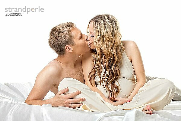 Junges glückliches Paar mit schwangerer Frau im Bett küssen zusammen