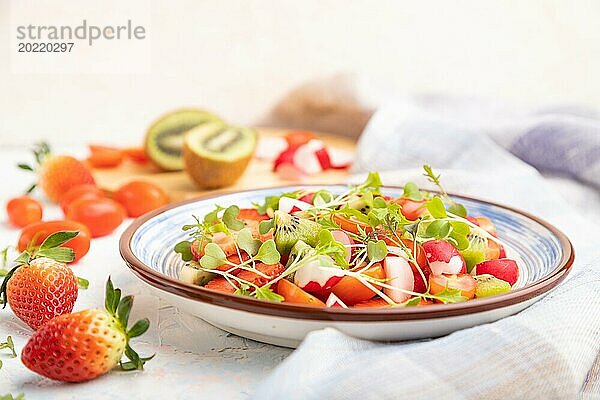 Vegetarischer Obst und Gemüsesalat aus Erdbeeren  Kiwi  Tomaten  Mikrogrünsprossen auf weißem Betonhintergrund und Leinentextil. Seitenansicht  Nahaufnahme  selektiver Fokus