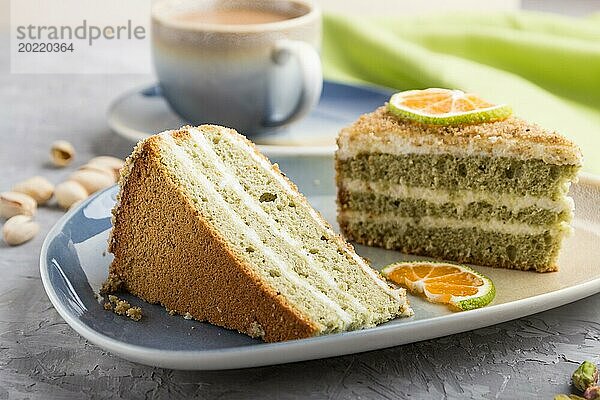 Hausgemachter Kuchen mit Milchcreme und Pistazien mit einer Tasse Kaffee auf einem grauen Betonhintergrund mit grünem Textil. Seitenansicht  Nahaufnahme  selektiver Fokus