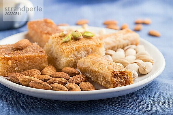 Traditionelle arabische Süßigkeiten (Basbus  Kunafa  Baklava)  eine Tasse Kaffee und Nüsse auf grauem Betonhintergrund und blauem Textil. Seitenansicht  Nahaufnahme  selektiver Fokus