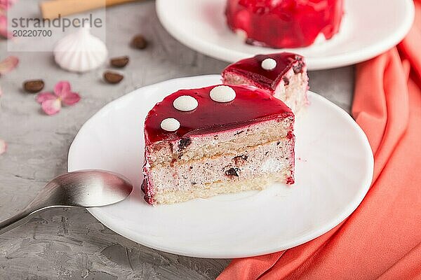 Geschnittener roter Kuchen mit Soufflé Creme und einer Tasse Kaffee auf grauem Betonhintergrund und rotem Textil. Seitenansicht  Nahaufnahme