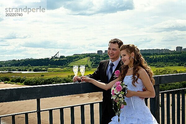 Hochzeitspaar in sonnigen Sommertag stehen auf Brücke mit Glas