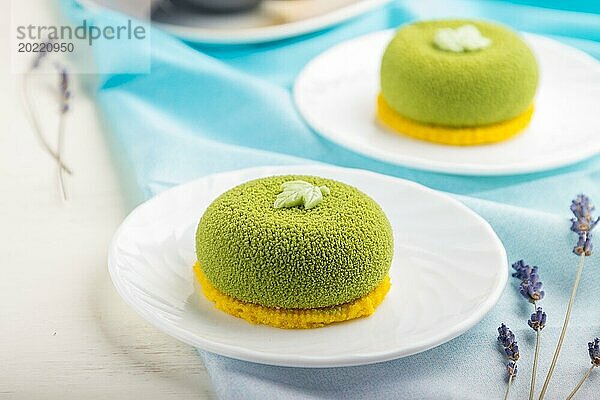 Grüner Mousse Kuchen mit Pistaziencreme und einer Tasse Kaffee auf einem weißen Holzhintergrund und blauem Stoff. Seitenansicht  Nahaufnahme  selektiver Fokus